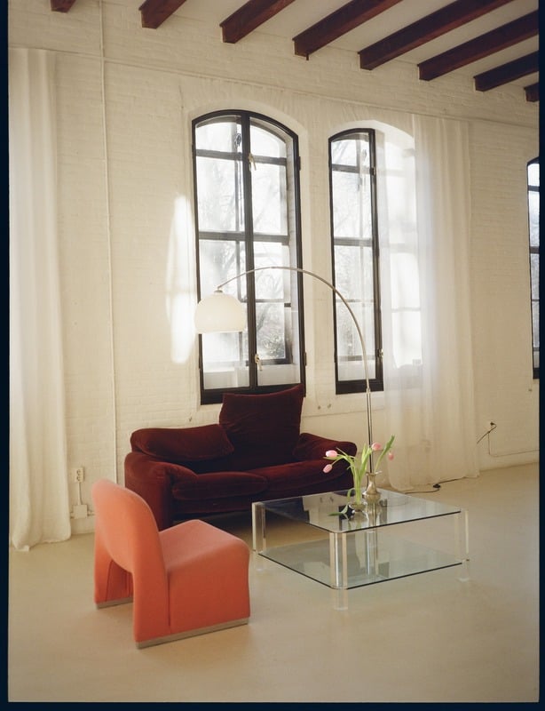 img7 Vintage lounge setup in Studio Mucha — rode fluwelen bank en koraal stoel bij twee originele fabrieksramen met daglicht.