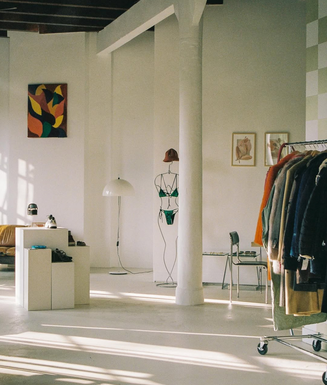 Brand activation styling in Studio Mucha eventlocatie — kledingrek met vintage jassen, kunstwerk en chrome staande lamp in de daglicht ruimte.