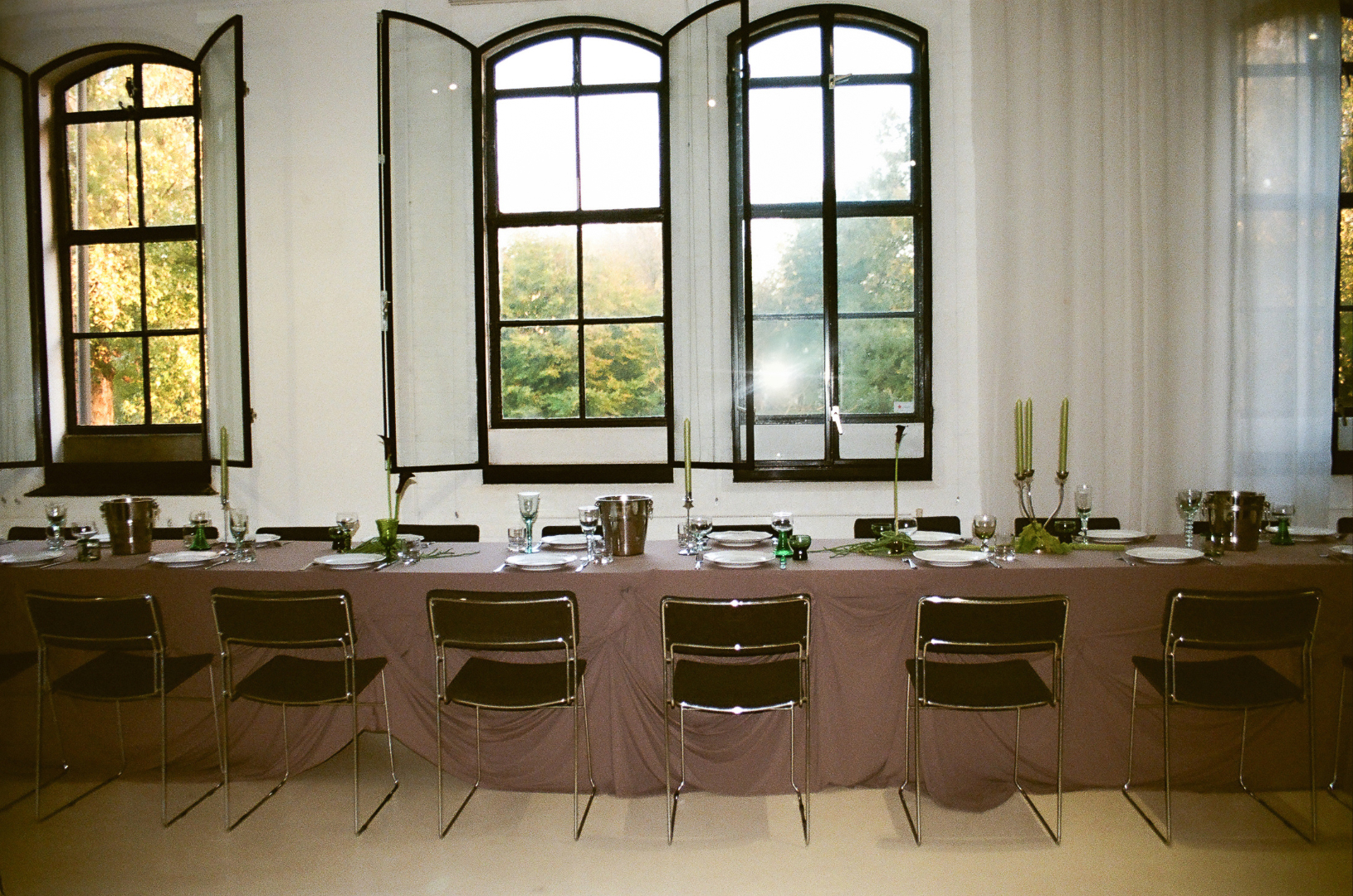 Untitled design – 1 Private dining setup in Studio Mucha eventlocatie Haarlem — lange tafel met chrome kandelaars, voor drie originele fabrieksramen.